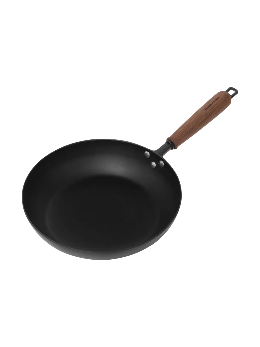 Musta taottu paistinpannu, jossa on pähkinäpuinen kahva ja ripustuslenkki.