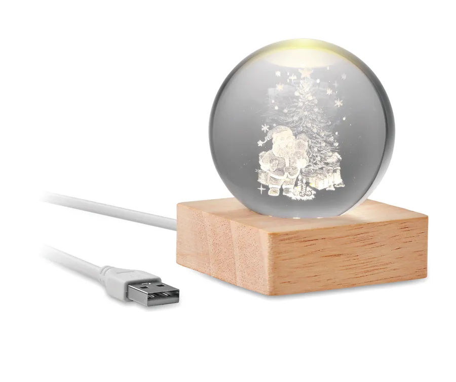 Lasipallo, jonka sisällä joulupukki ja kuusi, puisella jalustalla ja valkoisella USB-kaapelilla.