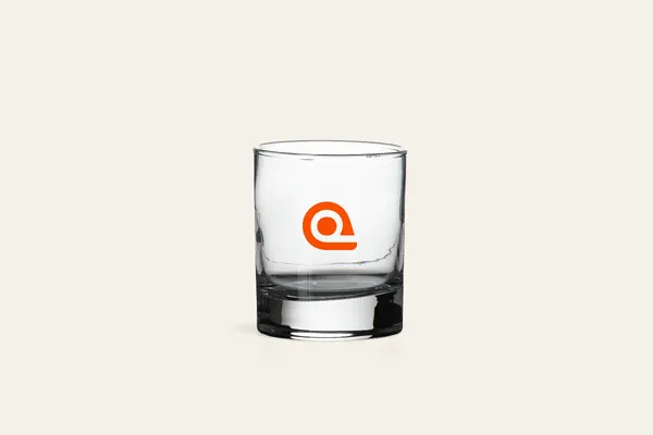 Kirkas 20 cl:n whiskylasi massiivisella pohjalla ja oranssilla logopainatuksella.