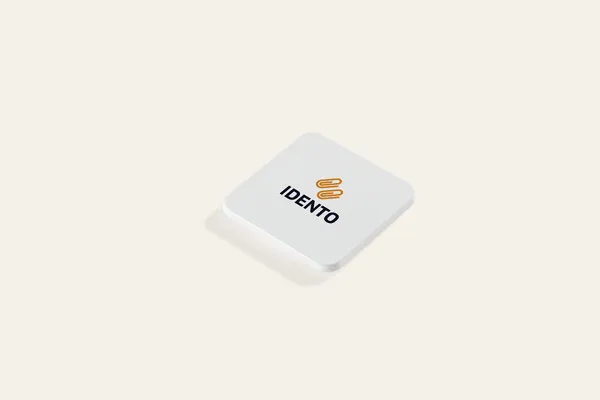 Valkoinen neliönmuotoinen jääkaappimagneetti, jossa esimerkkinä musta ja oranssi logopainatus.