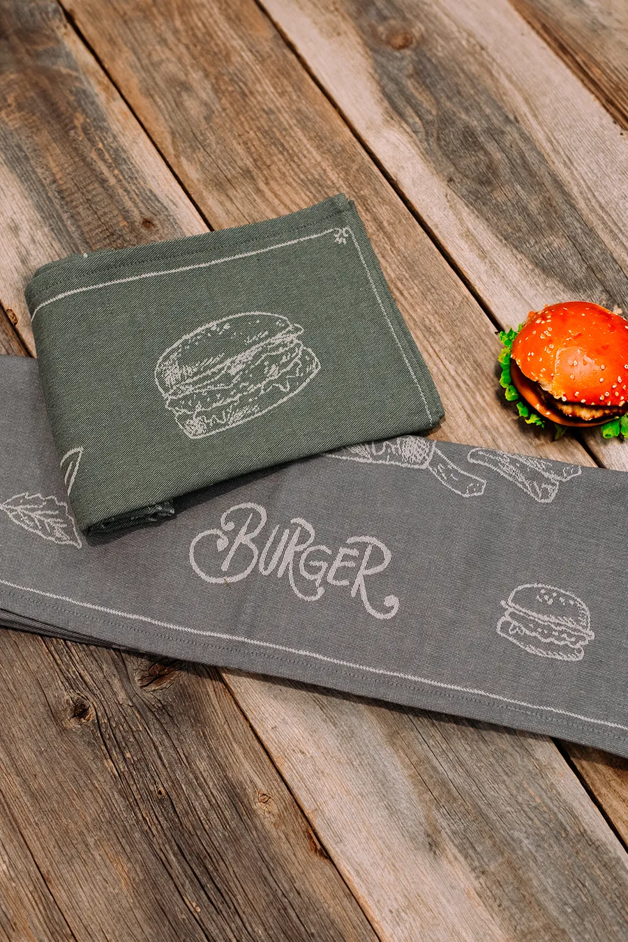 Harmaa Burger-keittiöpyyhe valkoisella burgeriaiheisella painatuksella
