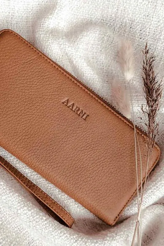 Ruskea hirvennahkainen clutch-lompakko, jonka pinnassa näkyy Aarni-logo.