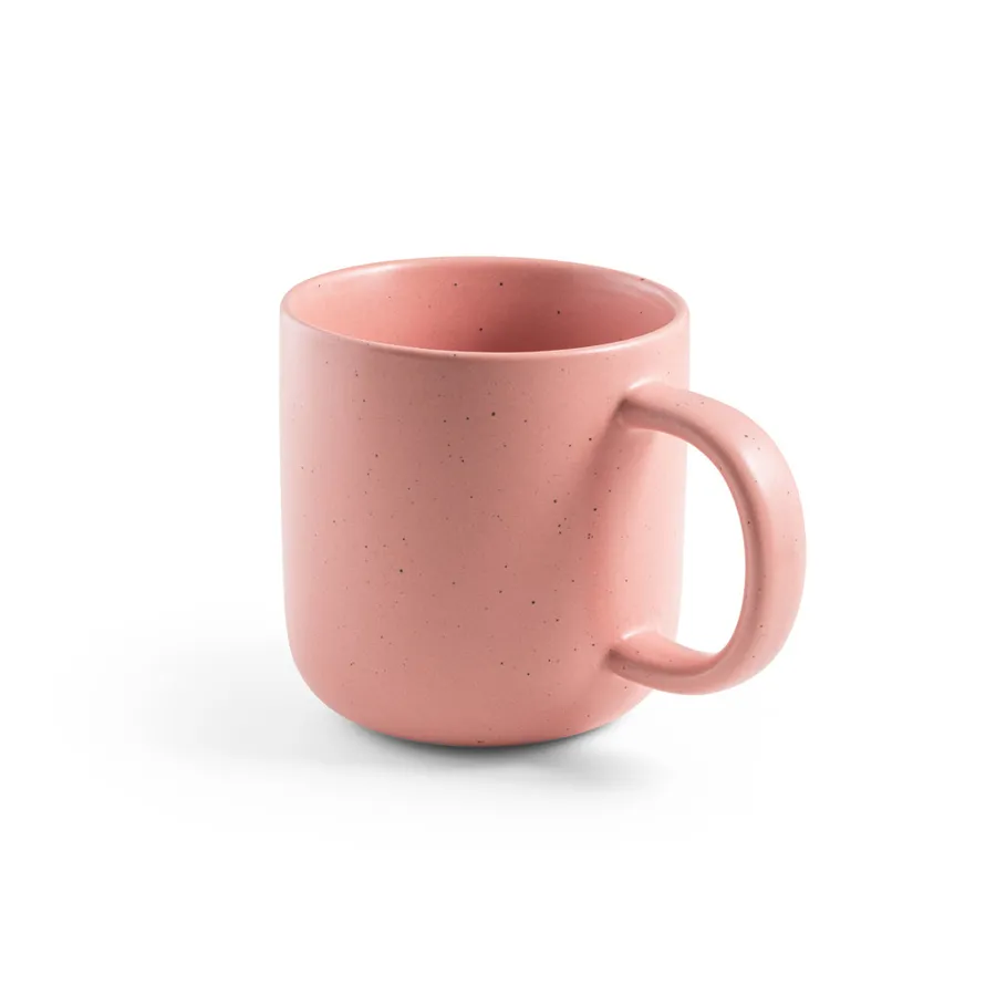 Vaaleanpunainen keraaminen muki, jossa on pyöreä korva ja pilkullinen pinta.
