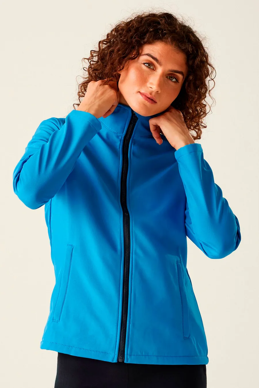 Sininen naisten softshell-takki, jossa etuvetoketju ja kaksi vetoketjutaskua.