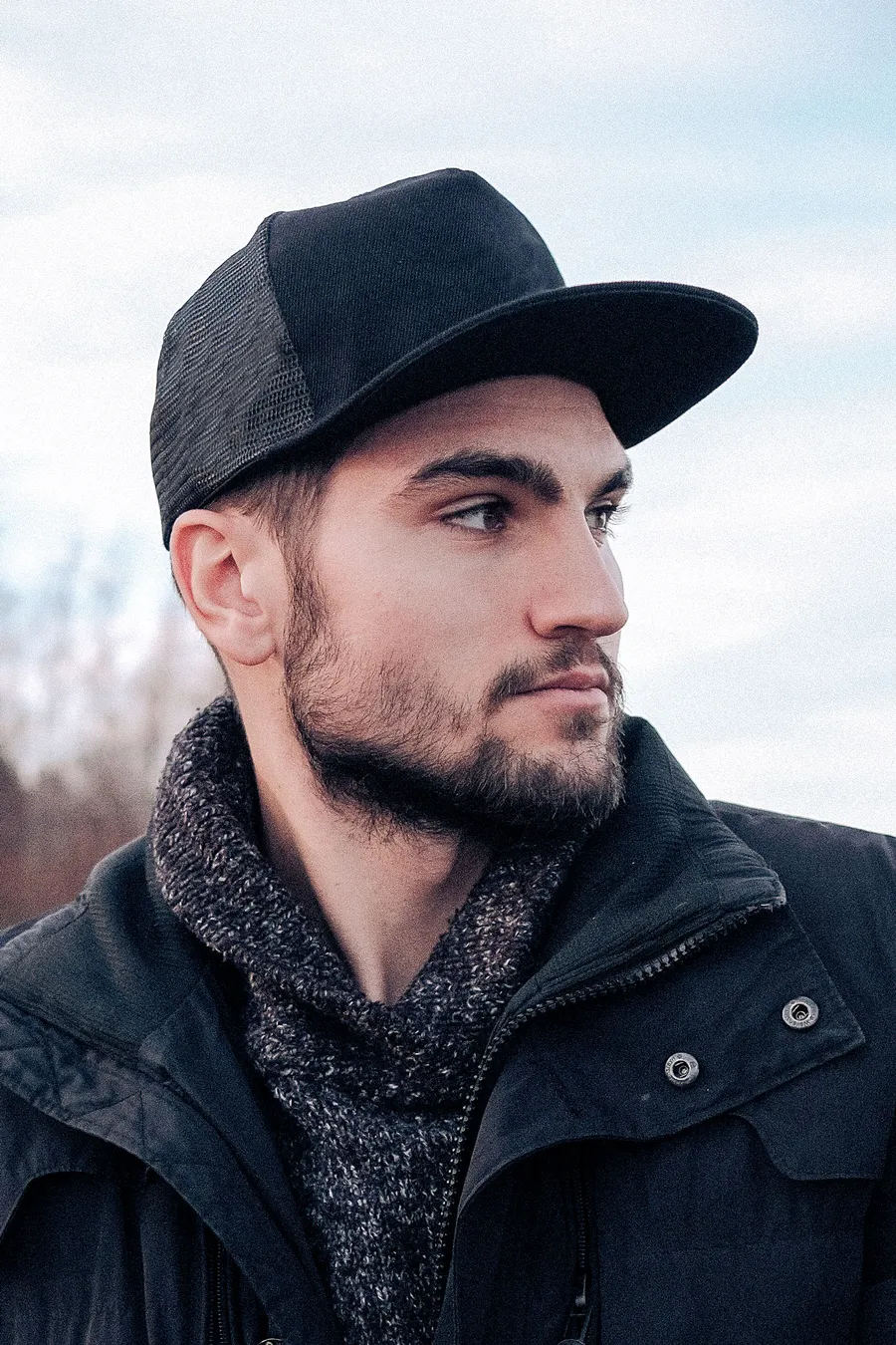 Musta Snapback Trucker -lippalakki verkkoperällä ja suoralla lipalla miehen päässä.