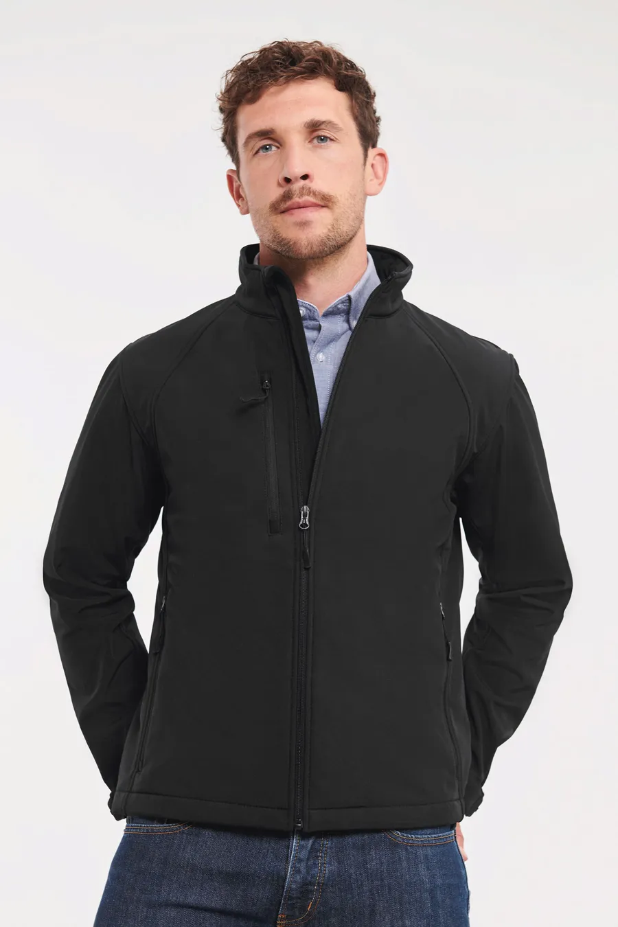 Miehellä musta softshell-takki, jossa korkea kaulus, etuvetoketju ja vetoketjullinen rintatasku.