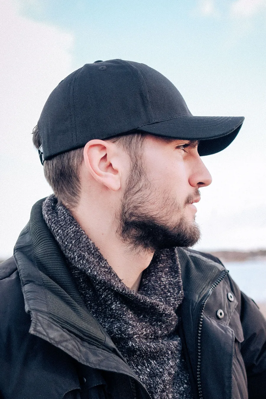 Mustaa 6-paneelista snapback-lippalakkia käyttävä mies sivulta kuvattuna.