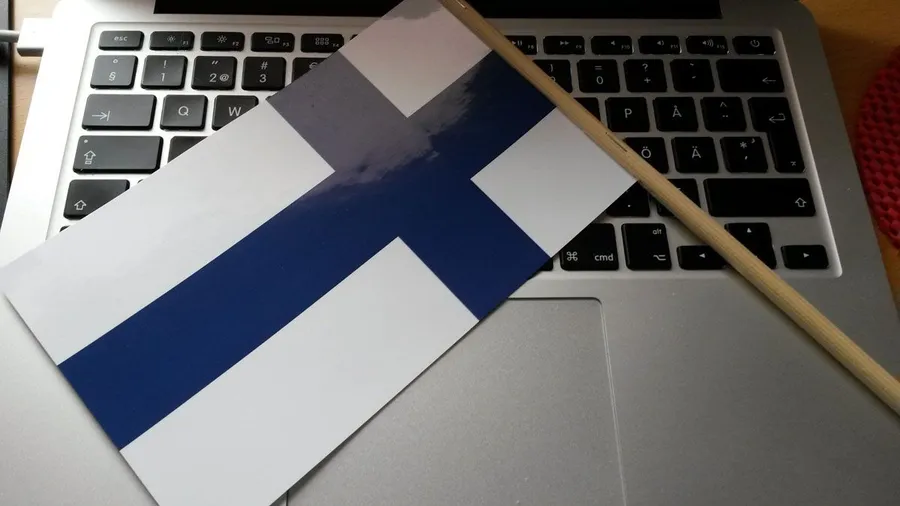 Finnish flag with pole on top of a laptop keyboard.